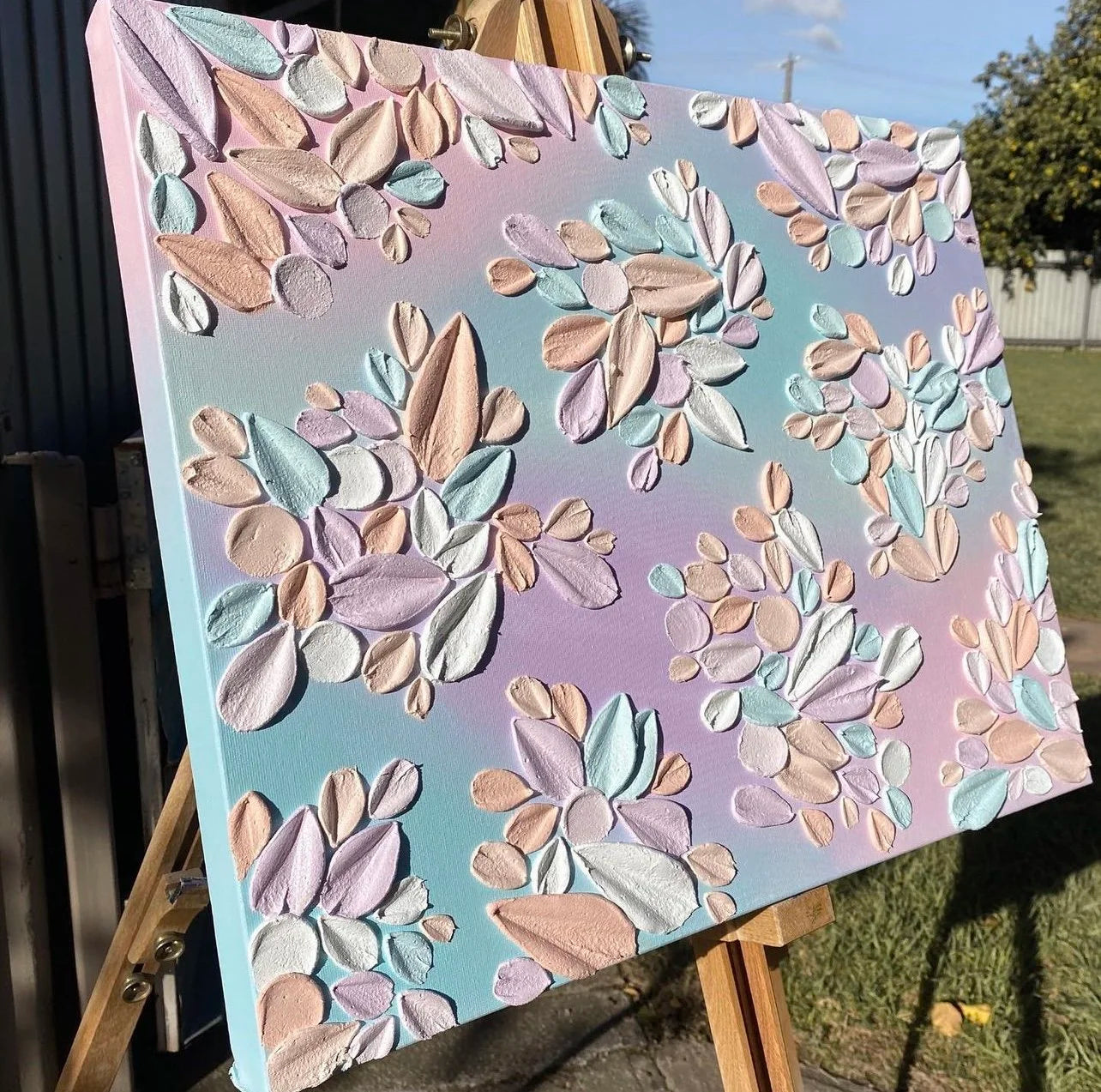 Pastel floral artwork on a canvas with a gradient background, displayed outdoors.