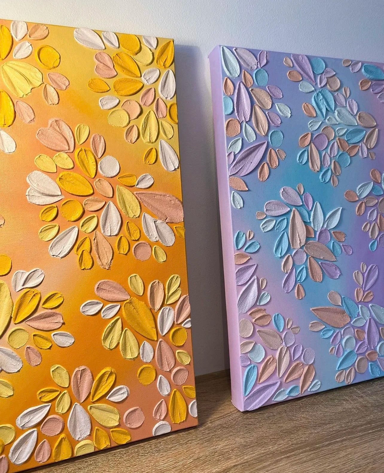 Two textured floral art pieces, one yellow and one blue, on a wooden surface.