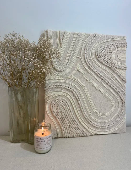 Textured wall art piece with a candle and vase on a light surface.