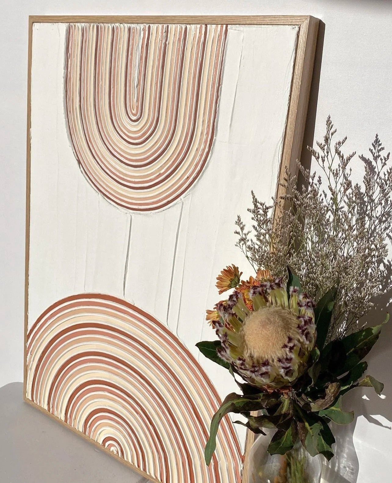 textured wall art with abstract circular patterns and a vase of flowers on a white surface.