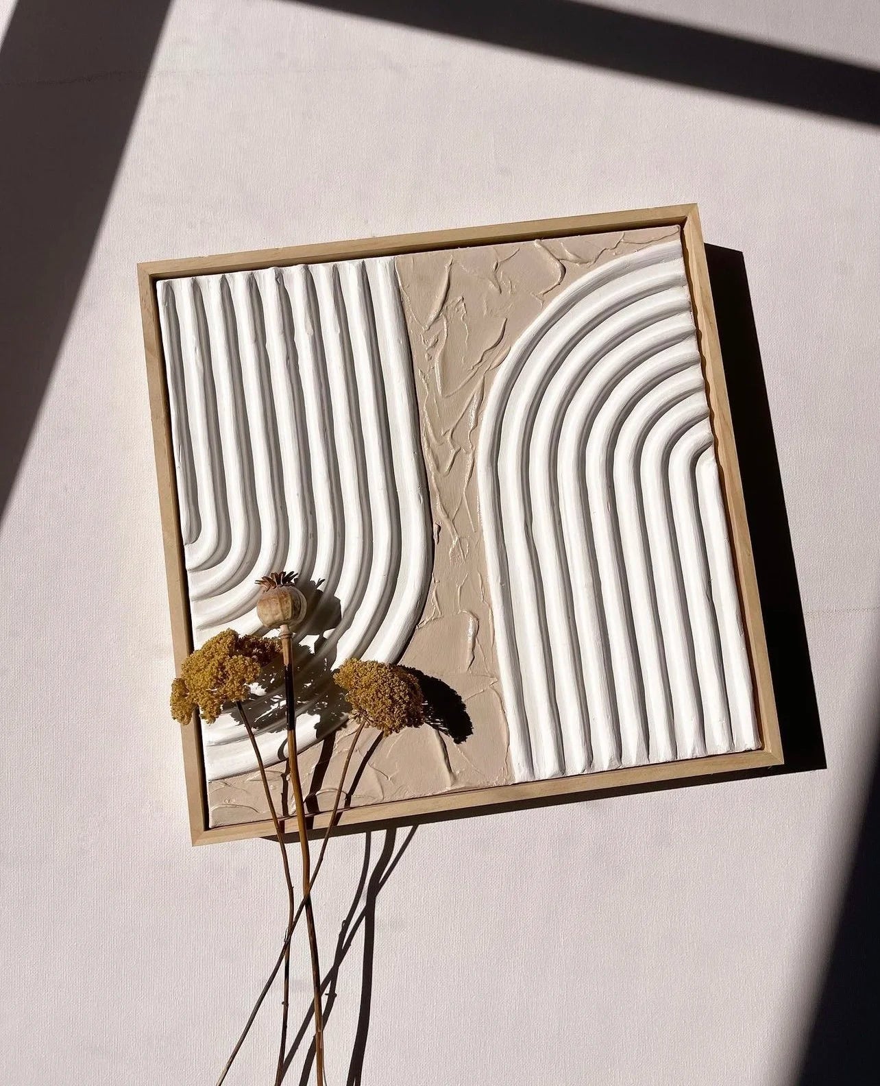 Decorative wall art with wavy lines and dried flowers on a neutral background