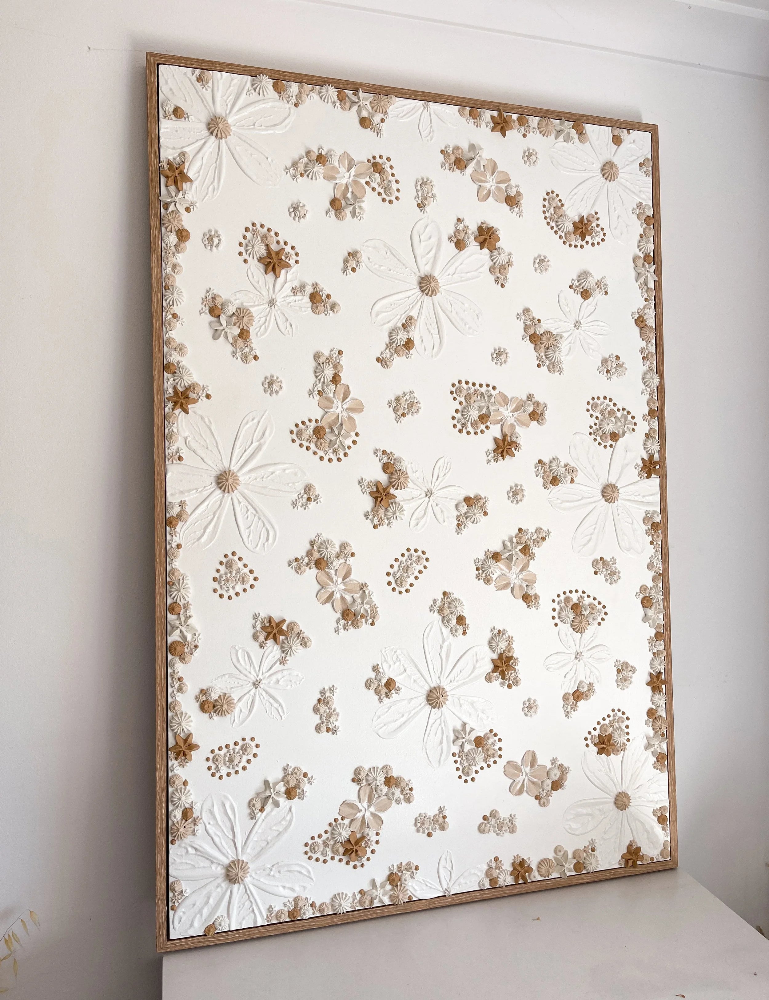 Textured artwork with floral pattern in a wooden frame on a white surface.