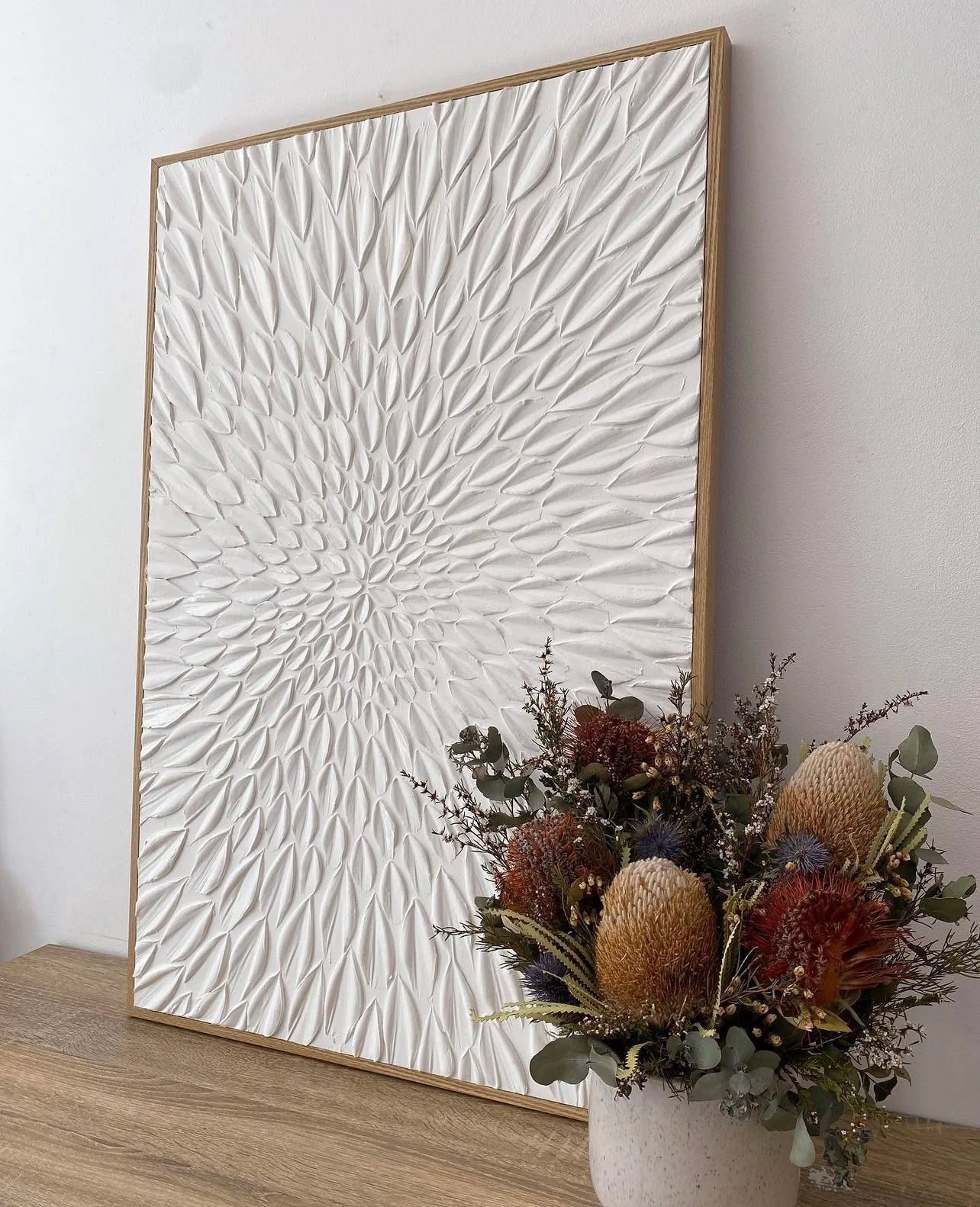 textured artwork with textured pattern on a wooden frame, placed on a surface with a vase of flowers.